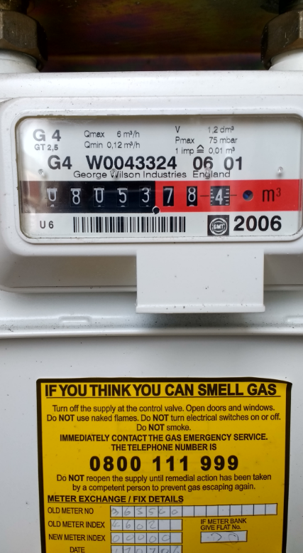 A white plastic gas meter showing several numbers in the viewing window and a black and red strip with several analogue numbers reading 08053 in black and 784 and red