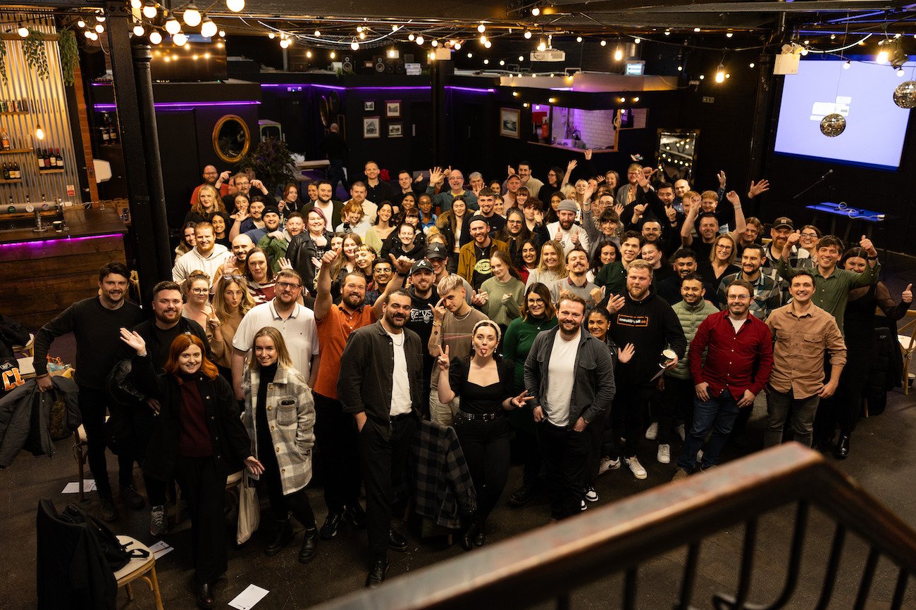 A group of about 100 people looking super happy after a One Utility Bill company update at Tyne Bank Brewery. There are string lights hanging about, it's clearly a good time.