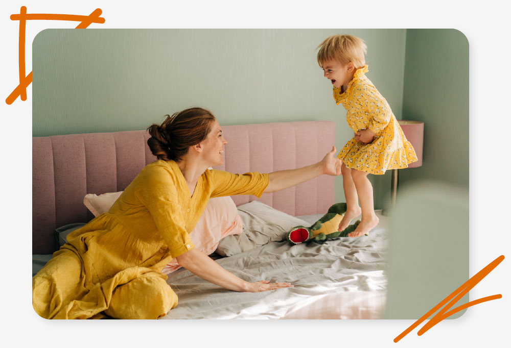 a woman and her toddler are happily bouncing on a bed, super warm because they got unlimited energy in their bills package