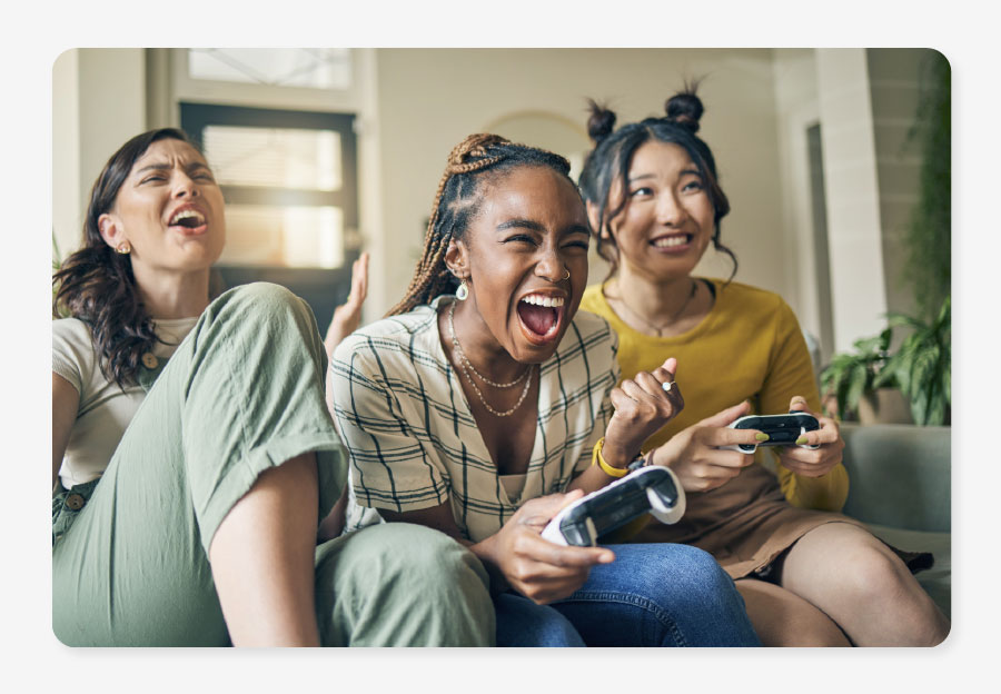 Three women playing on a games console excited and worry free because they got a superfast broadband deal in their One Utility Bill bills package.