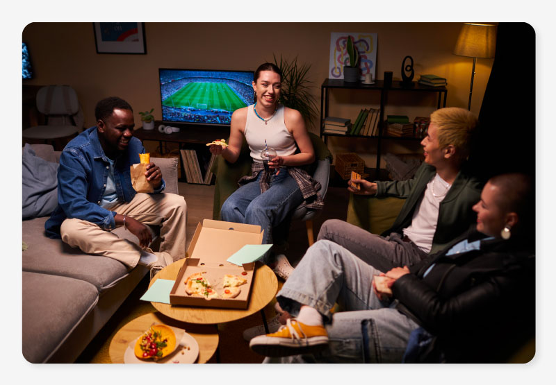 A group of friends gathered around eating a pizza with a football match on in the background thanks to their comprehensive Sky TV package