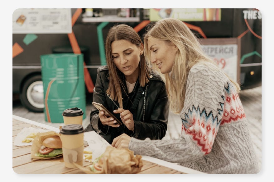 Two women sit eating burgers deciding which services to add to their easy bills package from One Utility Bill